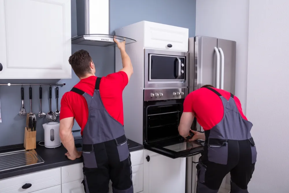 Repair specialists working on oven and range hood in Dubai kitchen.