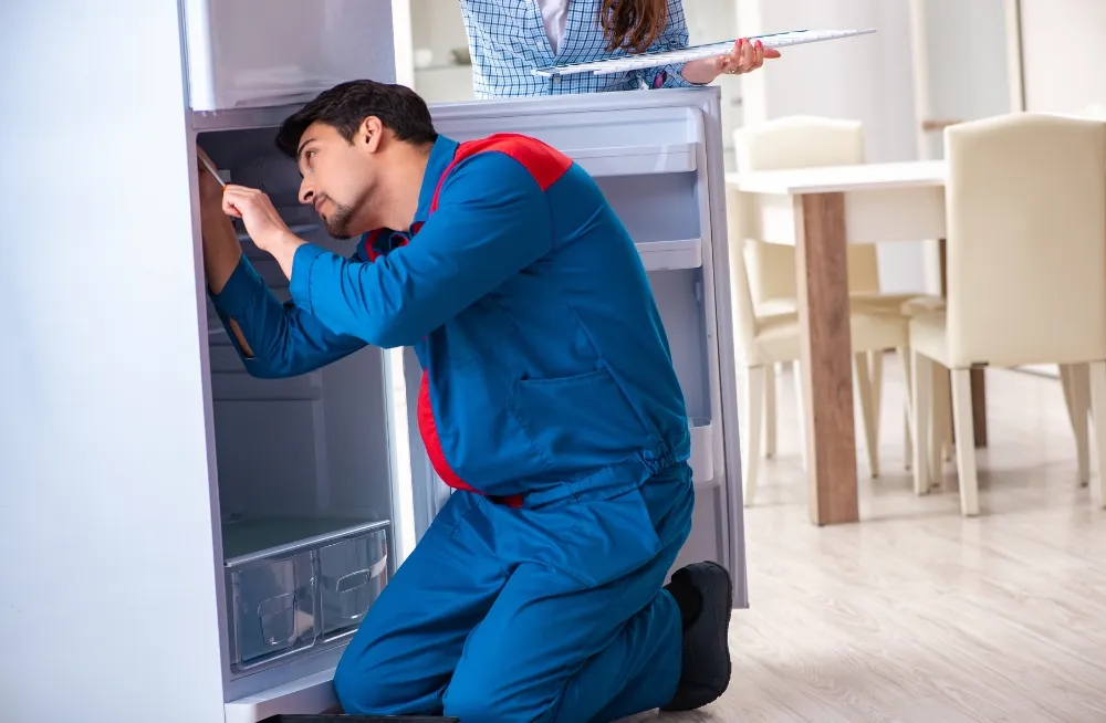 Fridge repair technician inspecting a commercial fridge while a customer looks on – Professional fridge repair services in Dubai.