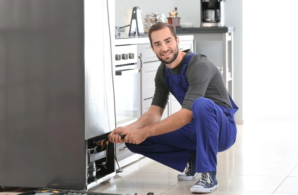 Smiling technician in Dubai repairing a refrigerator in a modern kitchen.